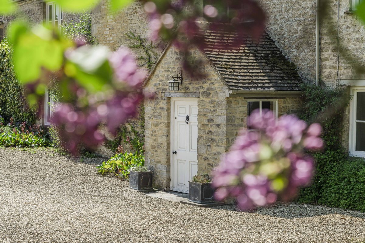 A stone porch with a white door at Purwell Farmhouse, framed by lilac blossom