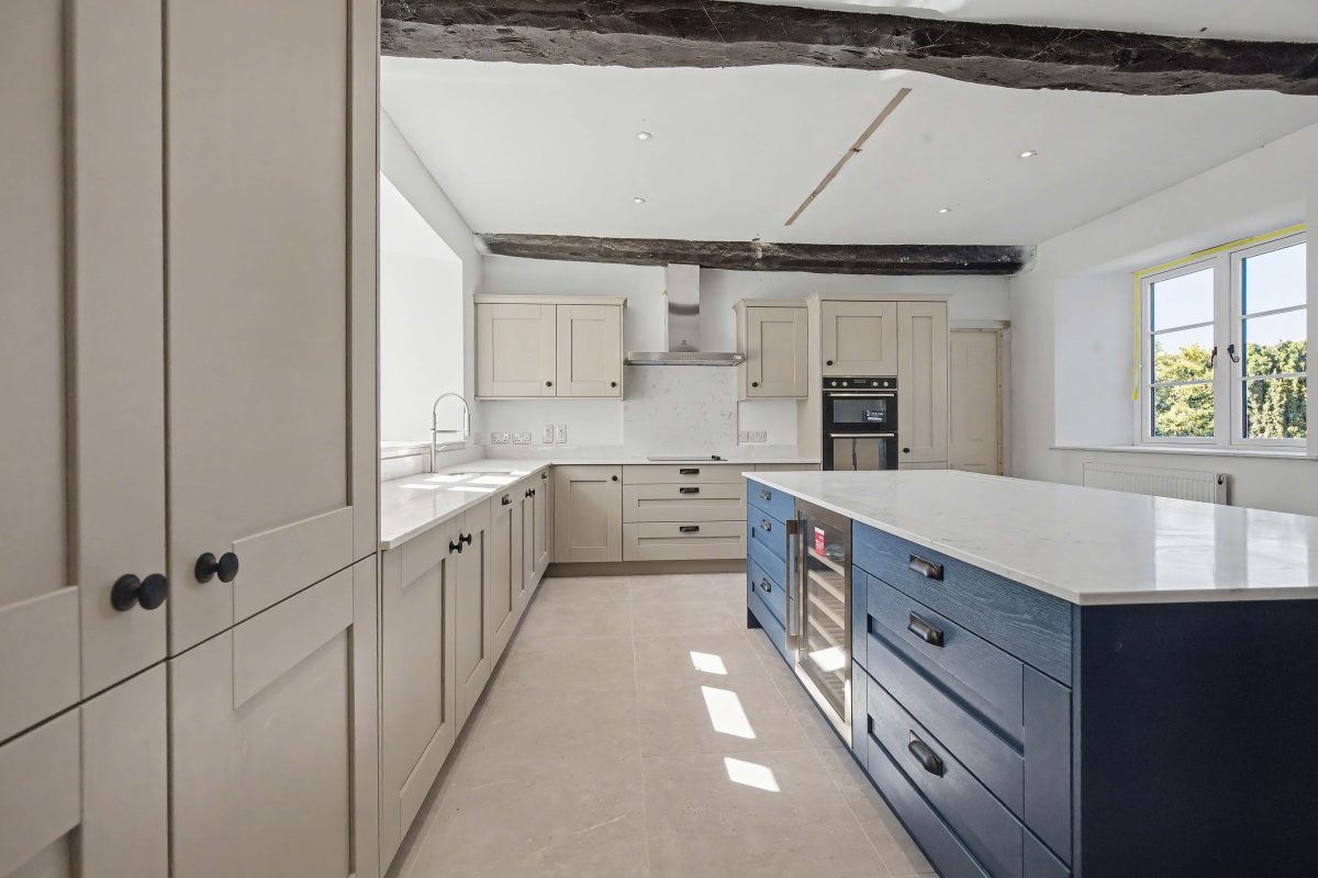 Kitchen at Purwell Farmhouse with cream units, a navy island and exposed ceiling beams