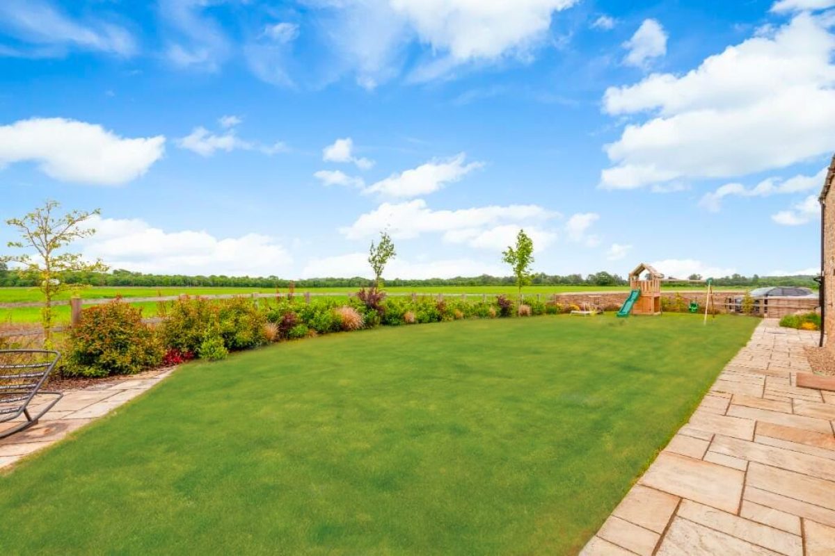 The garden at Littleworth Barn, a lawn with planted borders, a play frame and open fields beyond