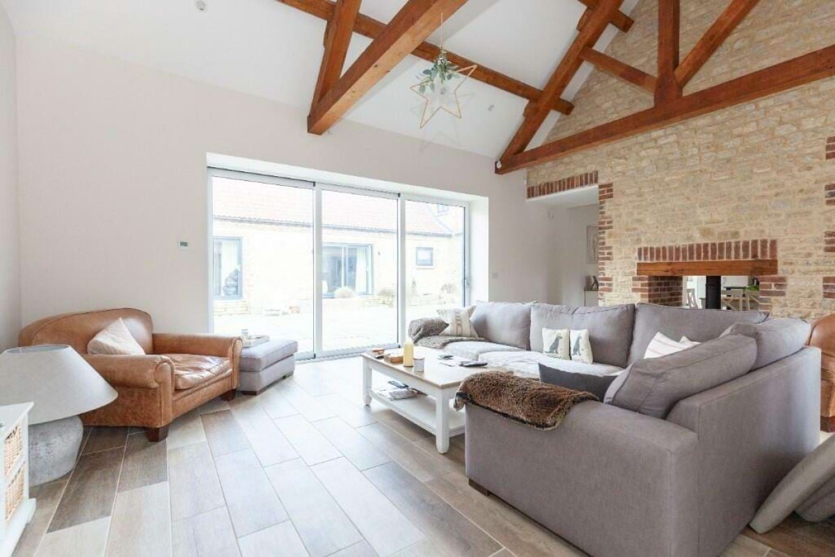 Living room at Hordley Farm Barns with grey sofas, oak trusses and sliding doors onto the courtyard