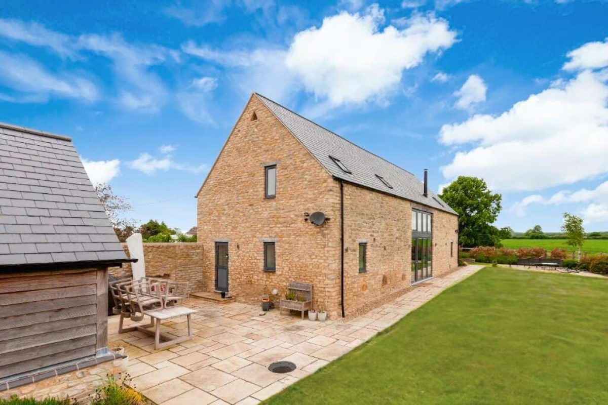 The rear of Littleworth Barn, with a paved terrace, lawn and timber outbuilding