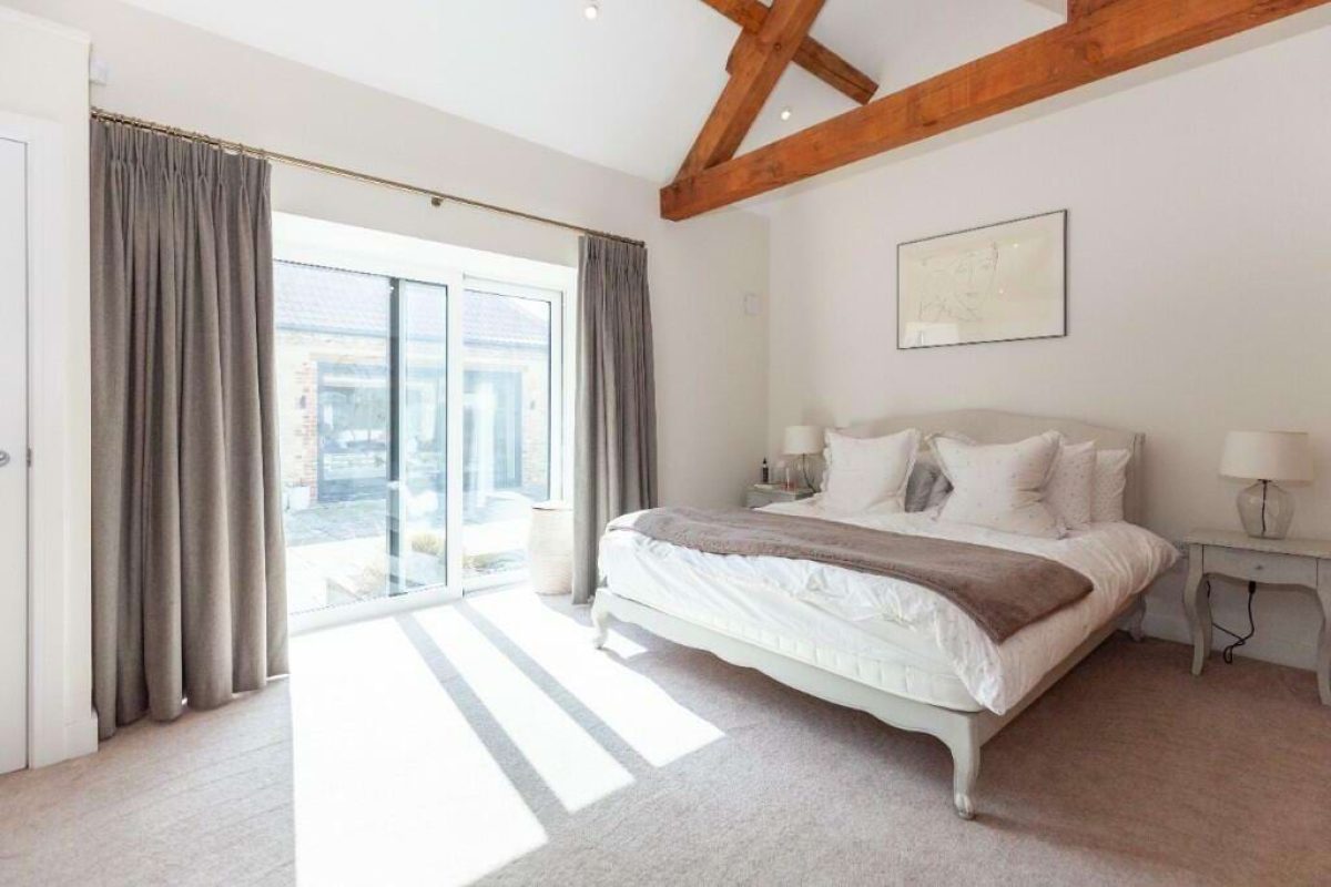 Bedroom at Hordley Farm Barns with a double bed, oak trusses and full-height glazing