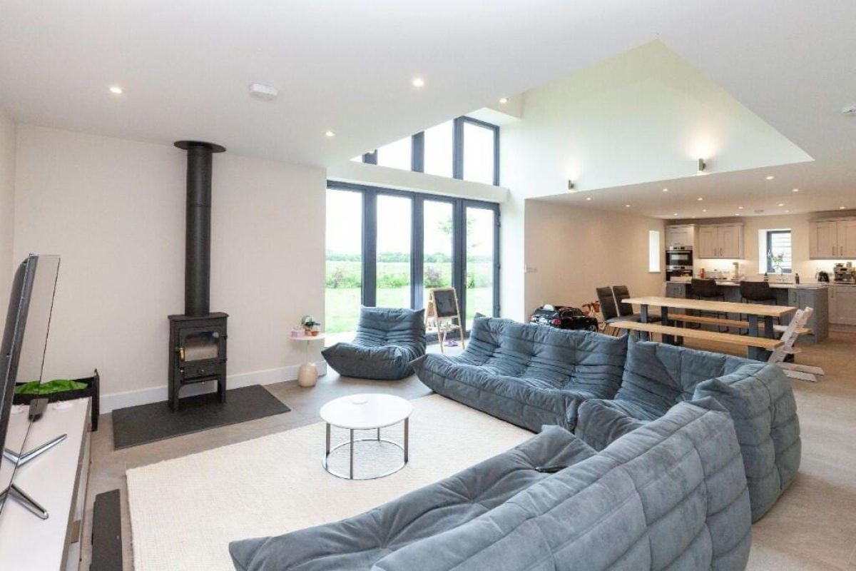 Open-plan living room at Littleworth Barn with a wood-burning stove, corner sofa and double-height windows