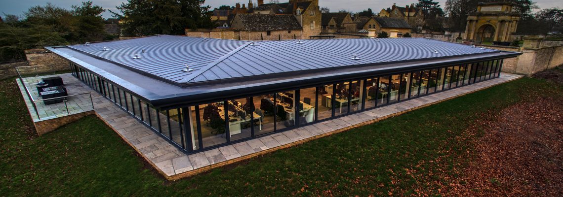 The Blenheim Estate Office, a low glass-walled building with a metal roof, with Woodstock behind at dusk