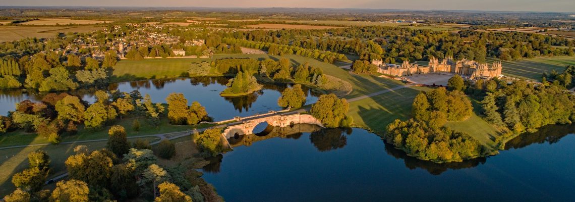 Aerial view of the lake and Grand Bridge at Blenheim at sunset, with the Palace and Woodstock beyond