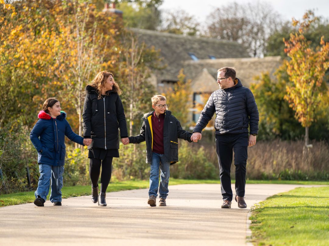 A family of four walking hand in hand along a path at Park View on an autumn day