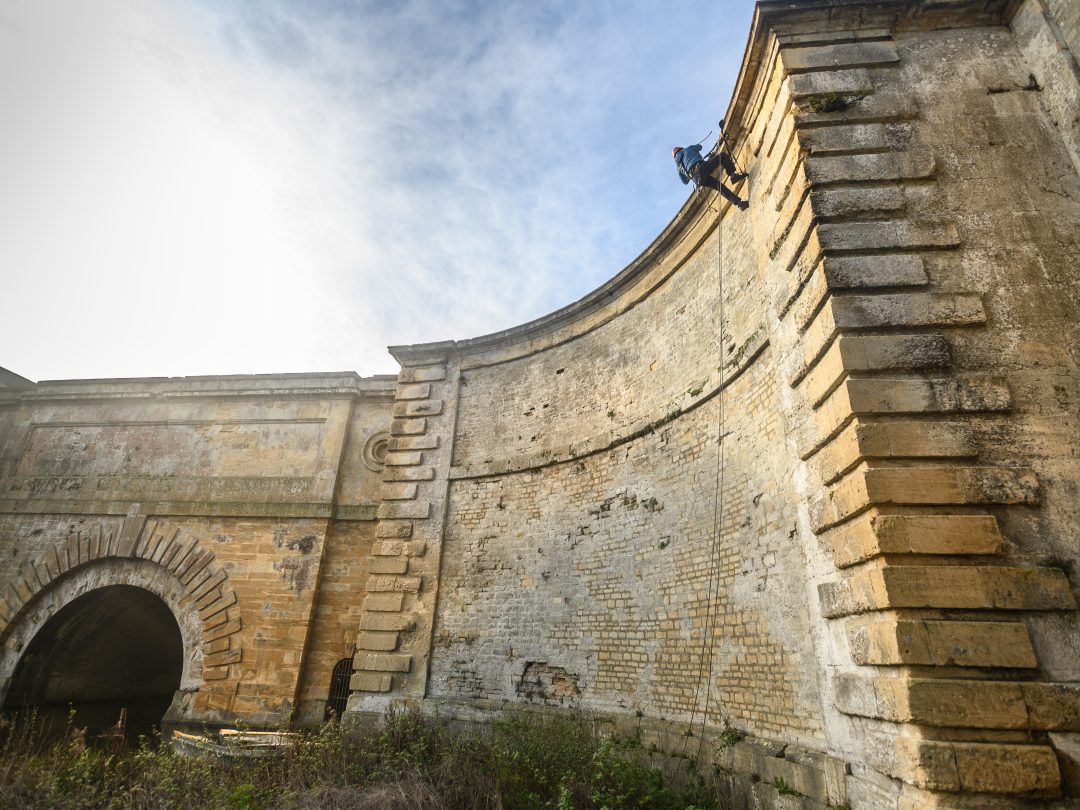 An ecologist on ropes high on the stone wall of the Grand Bridge, seen from below