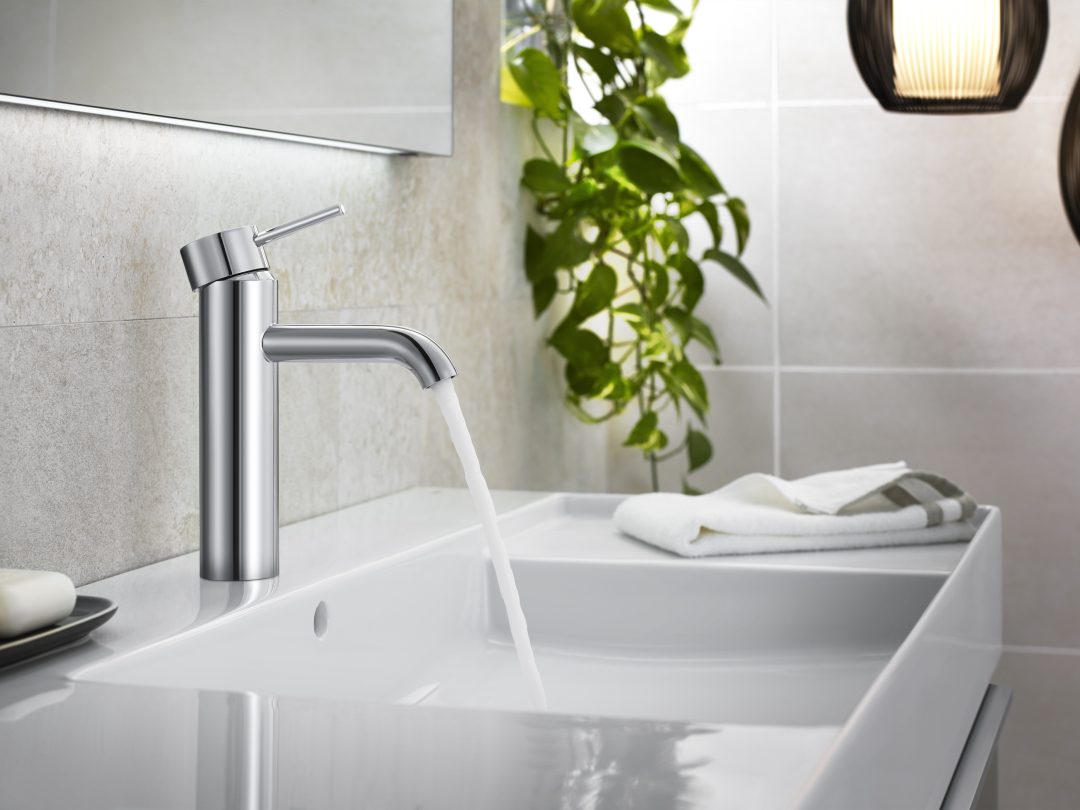 Chrome basin tap running into a white sink, with a hand towel and a trailing plant