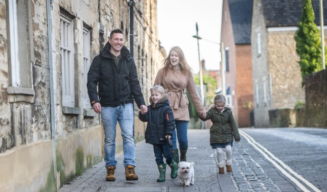 A family with two children and a small white dog walking along a stone-walled street in Woodstock