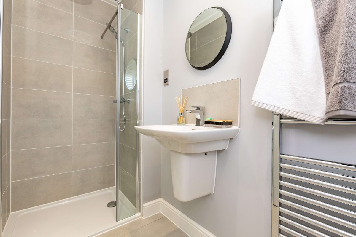 Shower room with a glass shower enclosure, wall-hung basin, round mirror and heated towel rail