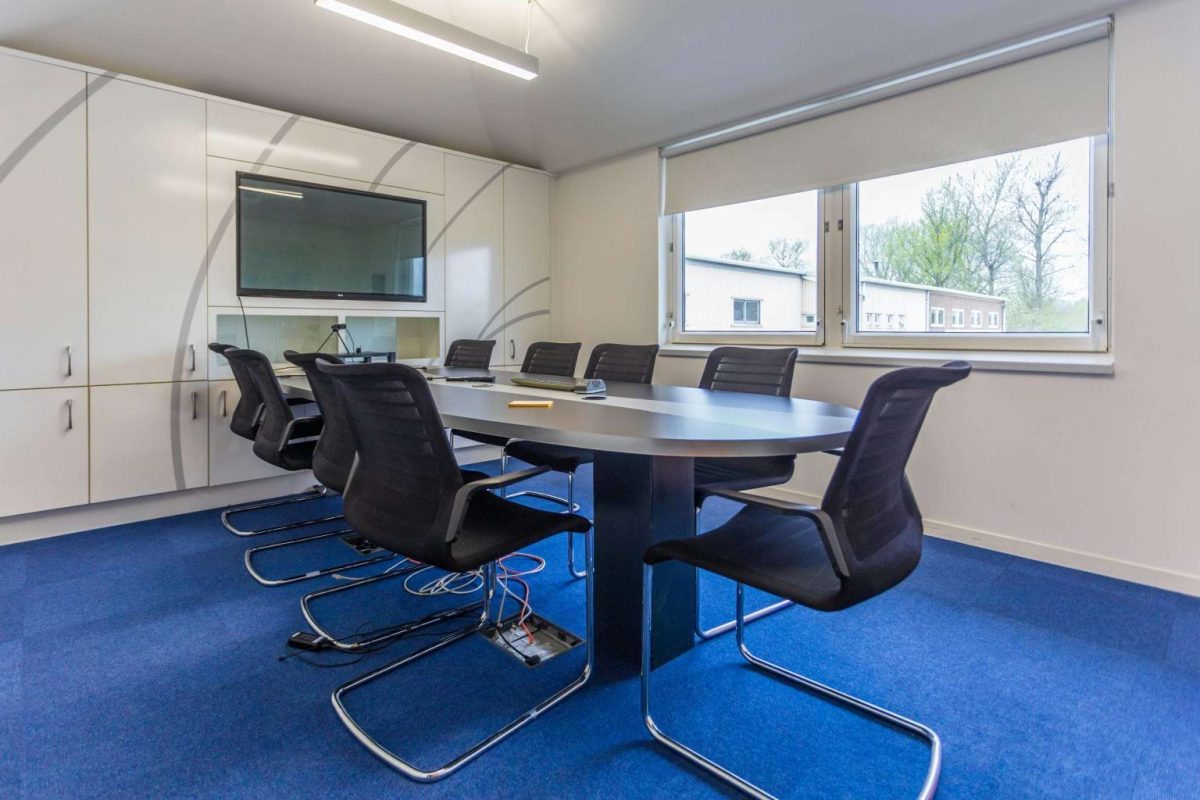 Meeting room at Brook Hill with an oval table, black chairs, blue carpet and a wall-mounted screen