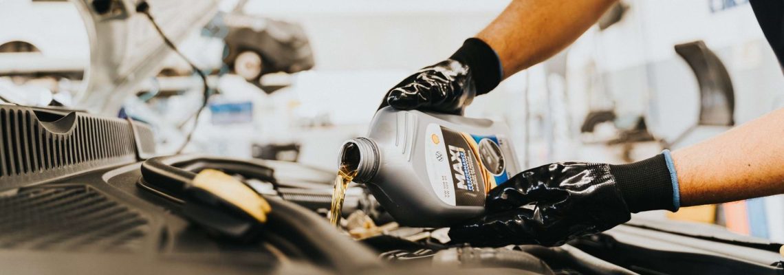 A mechanic in black gloves pouring engine oil into a car