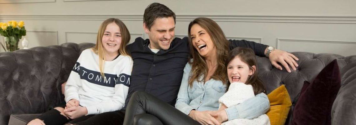 A family of four laughing together on a grey sofa in their new home at Park View