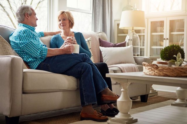 An older couple chatting on a sofa with mugs in a bright living room