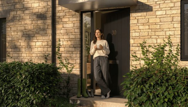 A woman holding a mug, leaning in the doorway of a stone home at Hill Rise