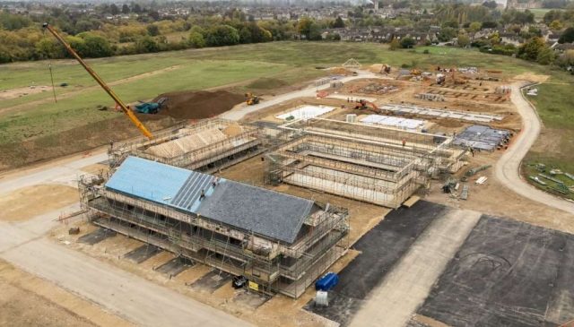 Aerial view of homes under construction at Hill Rise, with a crane and Woodstock beyond