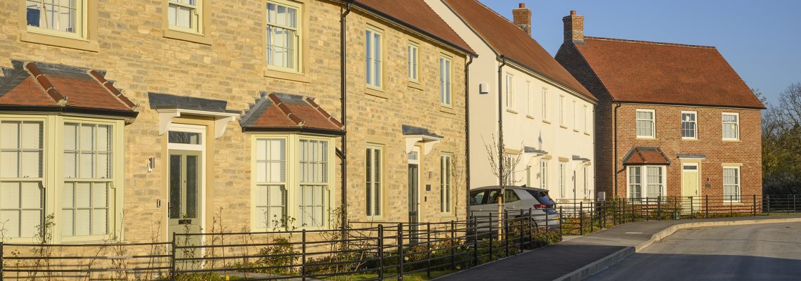 A row of stone, rendered and brick homes with bay windows and low metal railings along a street at Park View