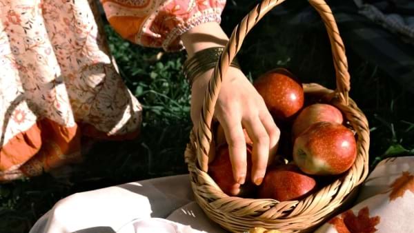 A hand picking red apples from a wicker basket
