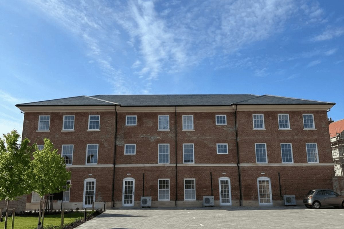 The Langley Apartments, a three-storey red-brick building with a paved parking court and young trees