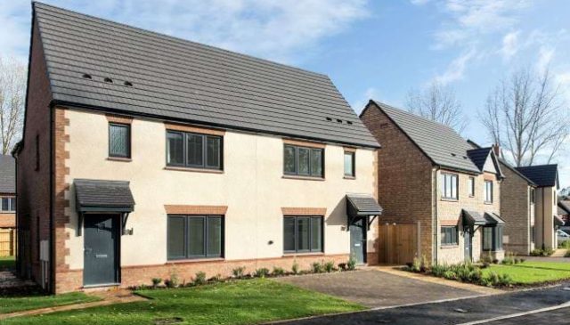 A pair of new semi-detached rendered homes with grey roofs and front lawns