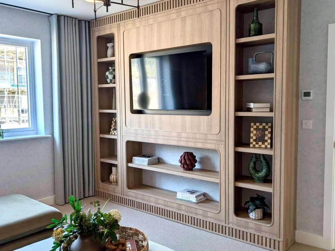 Living room in a Hill Rise show home with a wall of oak shelving around a television and a chandelier
