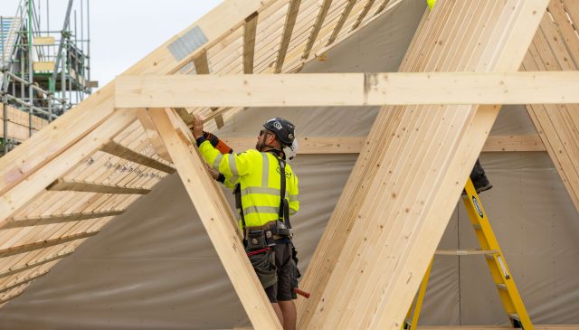 A construction worker in hi-vis fixing timber roof trusses on a new home