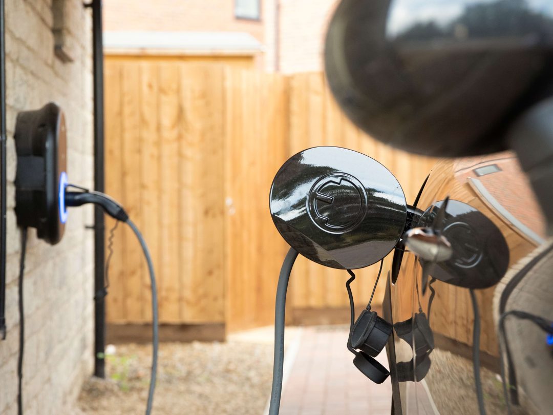 Close-up of an electric car charging cable plugged into a car beside a wall-mounted charger