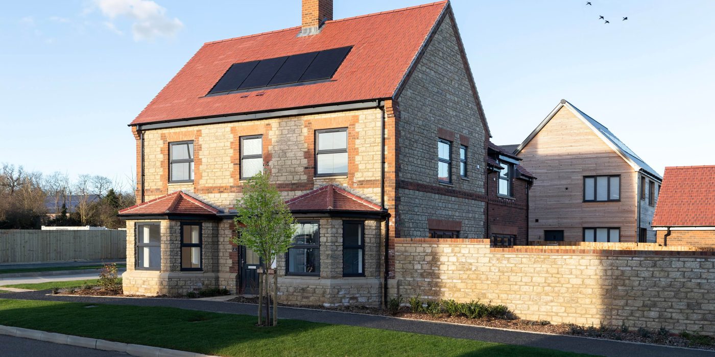 A detached stone home with a red tiled roof, solar panels and two bay windows at Church Farm