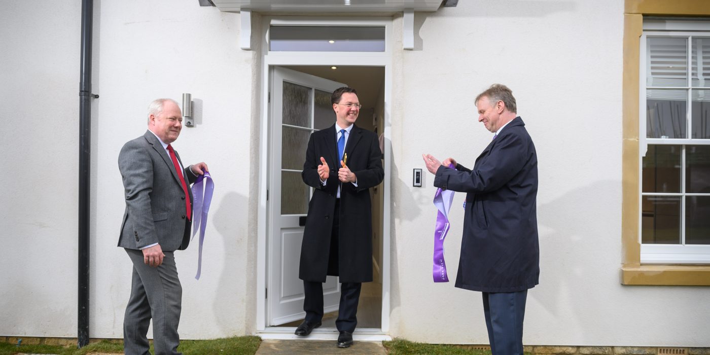 Three men applauding beside the front door of a new house after the ribbon is cut at Park View