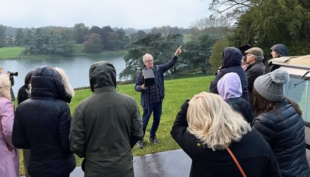 A guide pointing out across the lake to a group of photographers in Blenheim Park