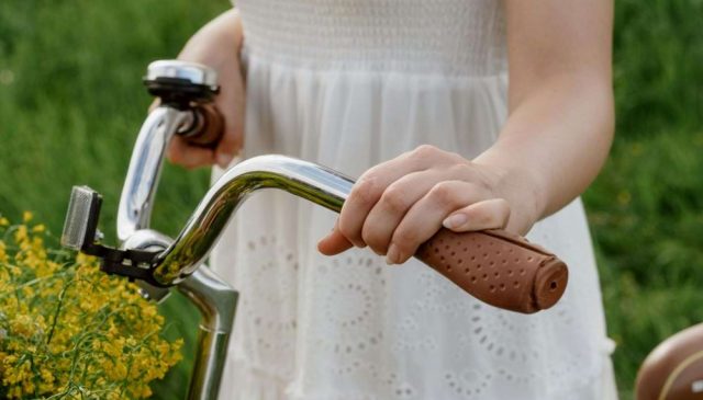 A woman in a white dress holding the handlebars of a vintage bicycle beside yellow wild flowers