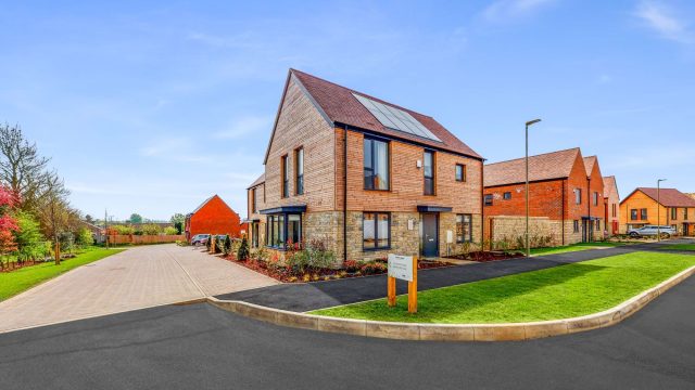 New timber-clad and brick homes with solar panels and a show home sign, by Pye Homes