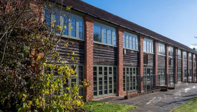 Exterior of the Sawmills offices, a long two-storey brick and timber-clad building with green-framed windows