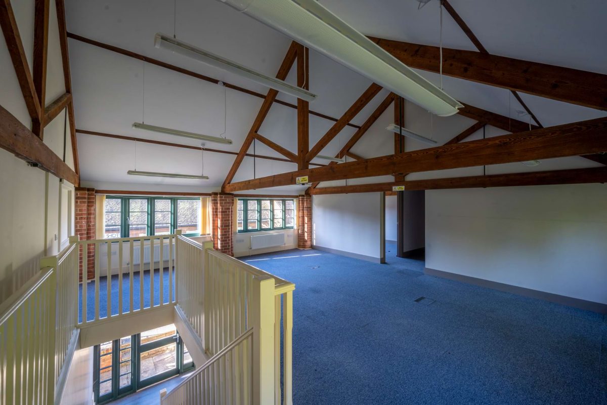 First-floor office at the Sawmills under exposed timber roof trusses, with a galleried stairwell