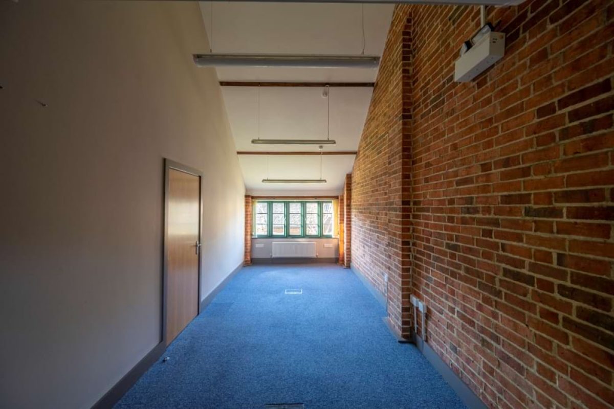 Long narrow office at the Sawmills with an exposed brick wall, blue carpet and a window at the far end