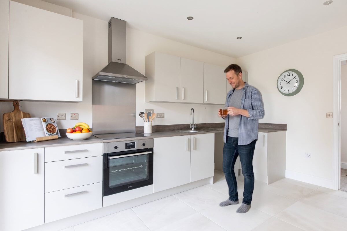 A man holding a mug in a white fitted kitchen with a built-in oven and extractor hood
