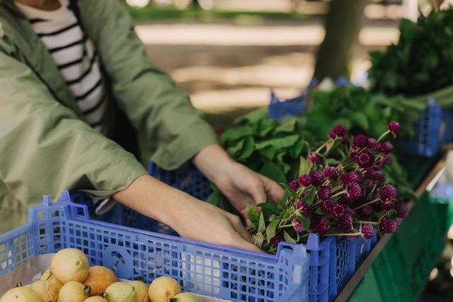 A person arranging fresh flowers and vegetables in blue crates on a market stall