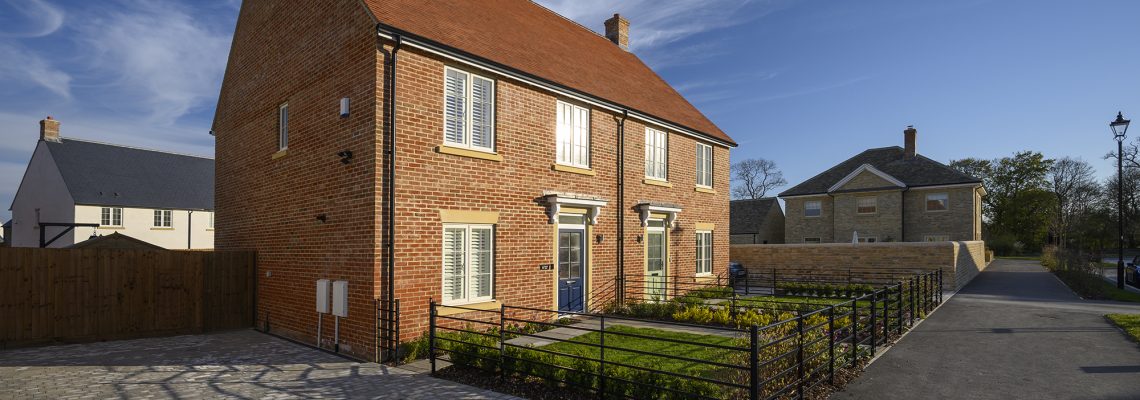 A detached red-brick house with a blue front door and black railings on a new street at Park View