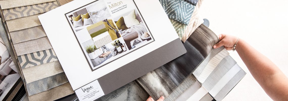 Hands turning the pages of a Vogue Showhomes interior design board among fabric samples