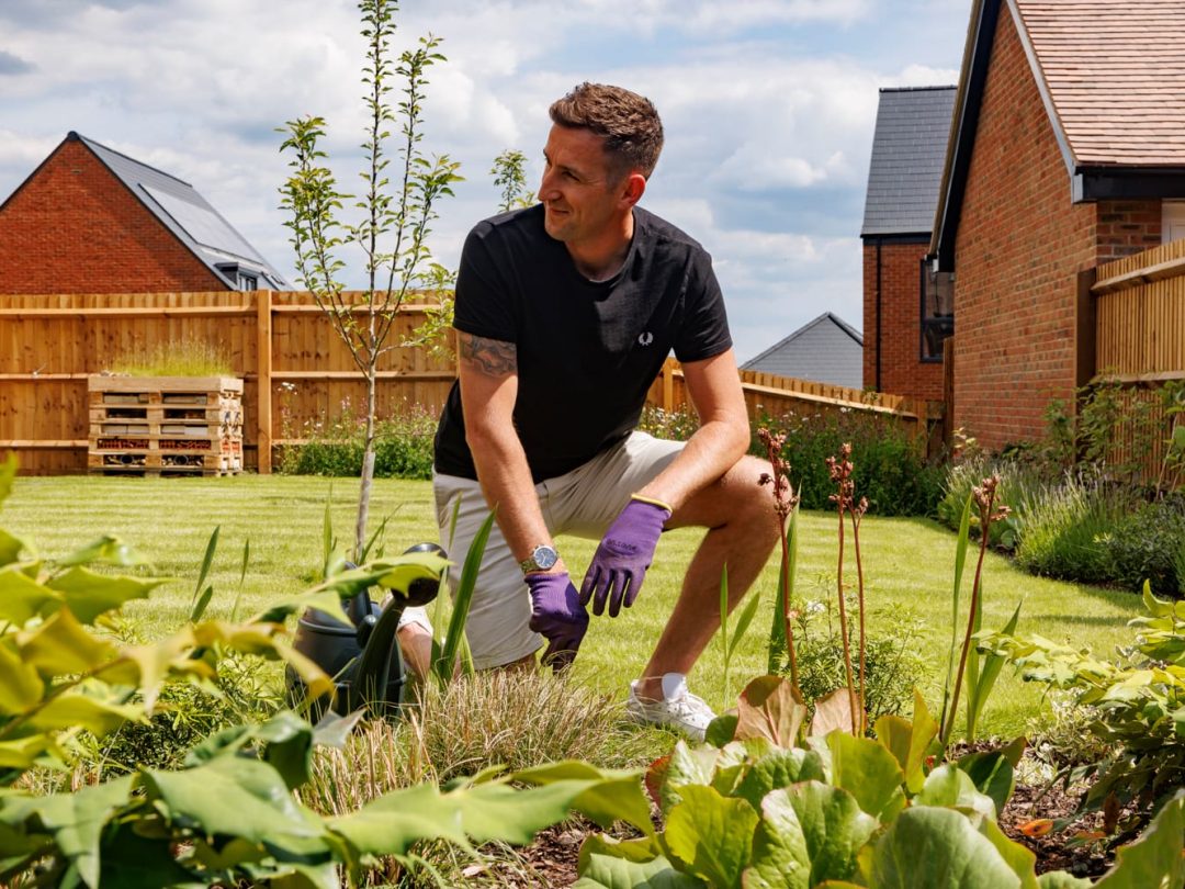 A man in gardening gloves kneeling to tend a planted border in a new garden at Church Farm