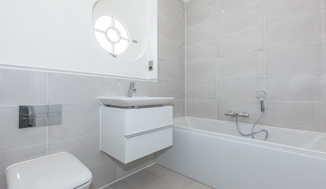 Bathroom with a wall-hung basin, concealed-cistern toilet, bath with a shower mixer and a round porthole window