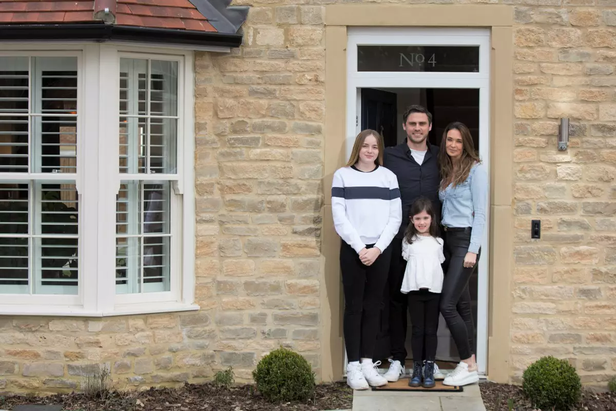 The Cooper family, two parents and two daughters, standing at the front door of their stone home at Park View